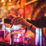 Midsection of a young female bartender preparing a cocktails in a nightlife cocktail bar. Selective focus. Focus on foreground.
